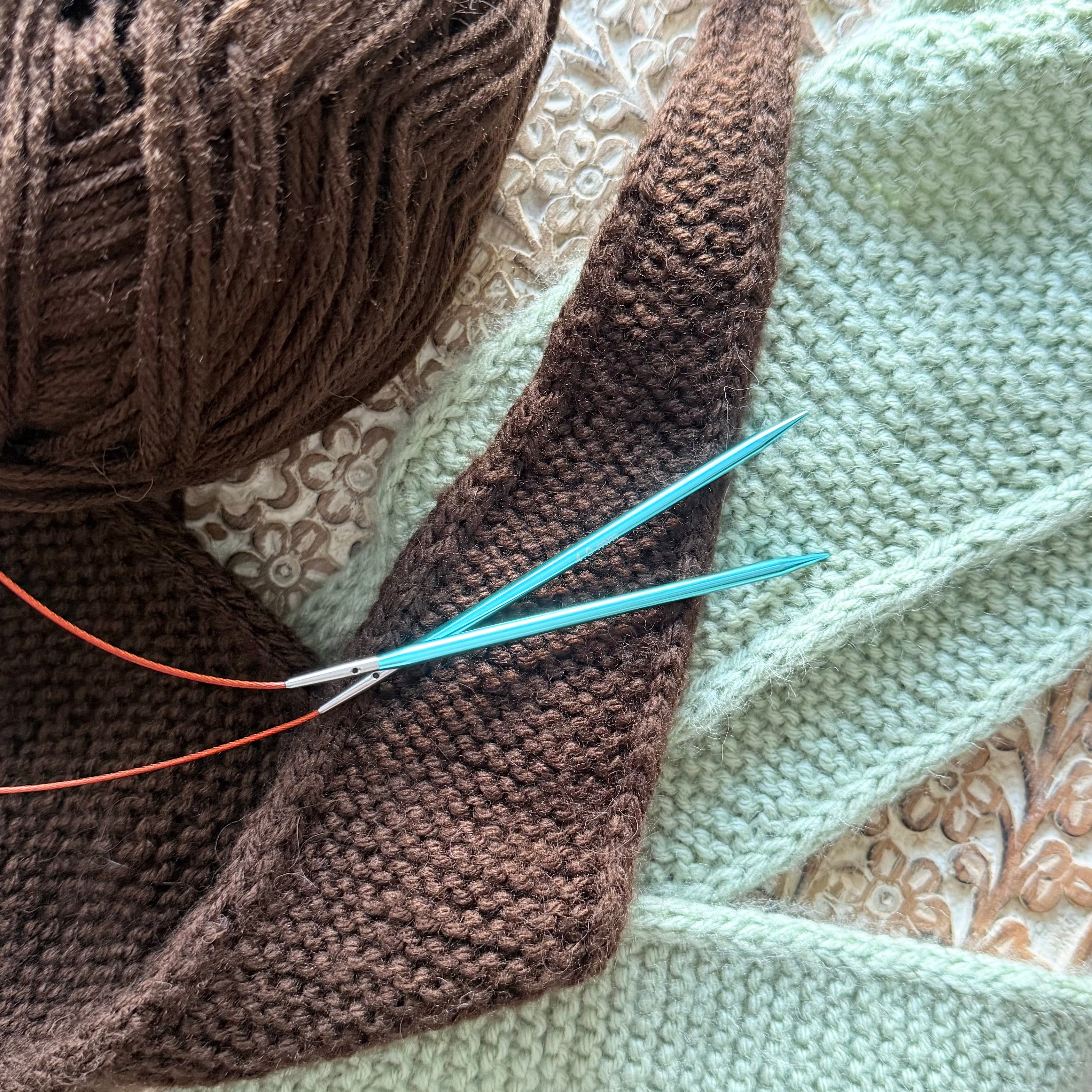 Knitting project with brown yarn and needles on a textured surface