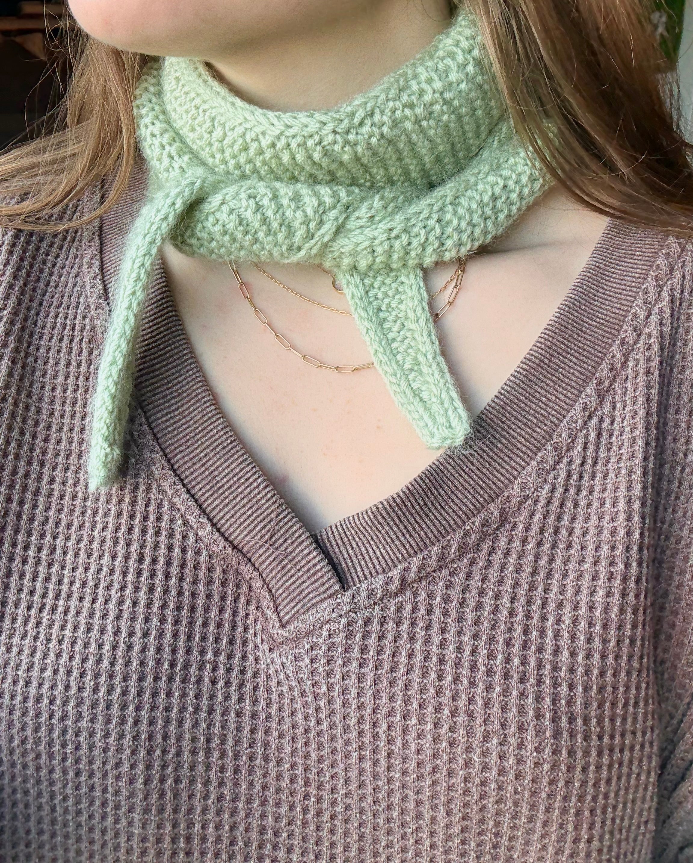 Person wearing a light green knitted scarf with a brown sweater