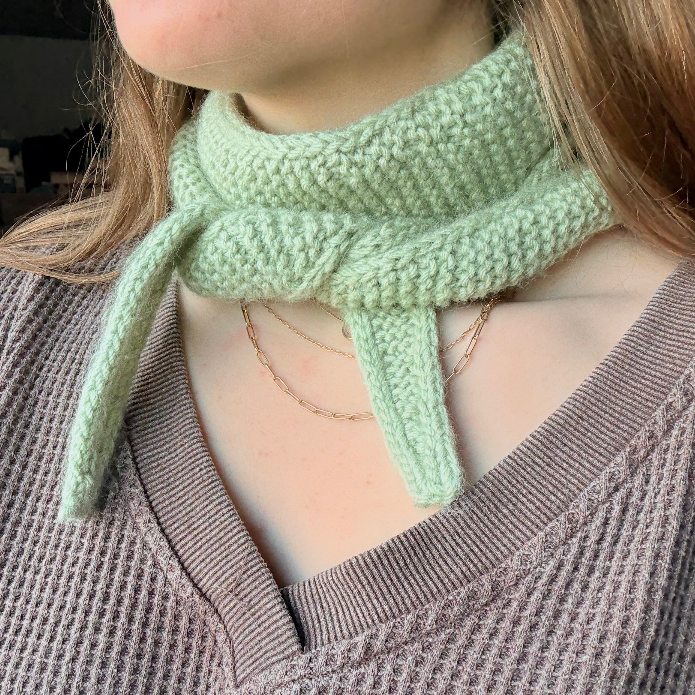 Person wearing a light green knitted scarf with a brown sweater