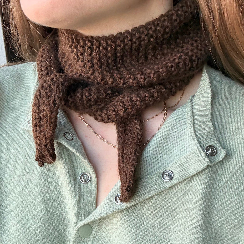 Person wearing a brown knitted scarf with a light green shirt