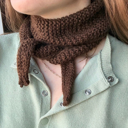 Person wearing a brown knitted scarf with a light green shirt