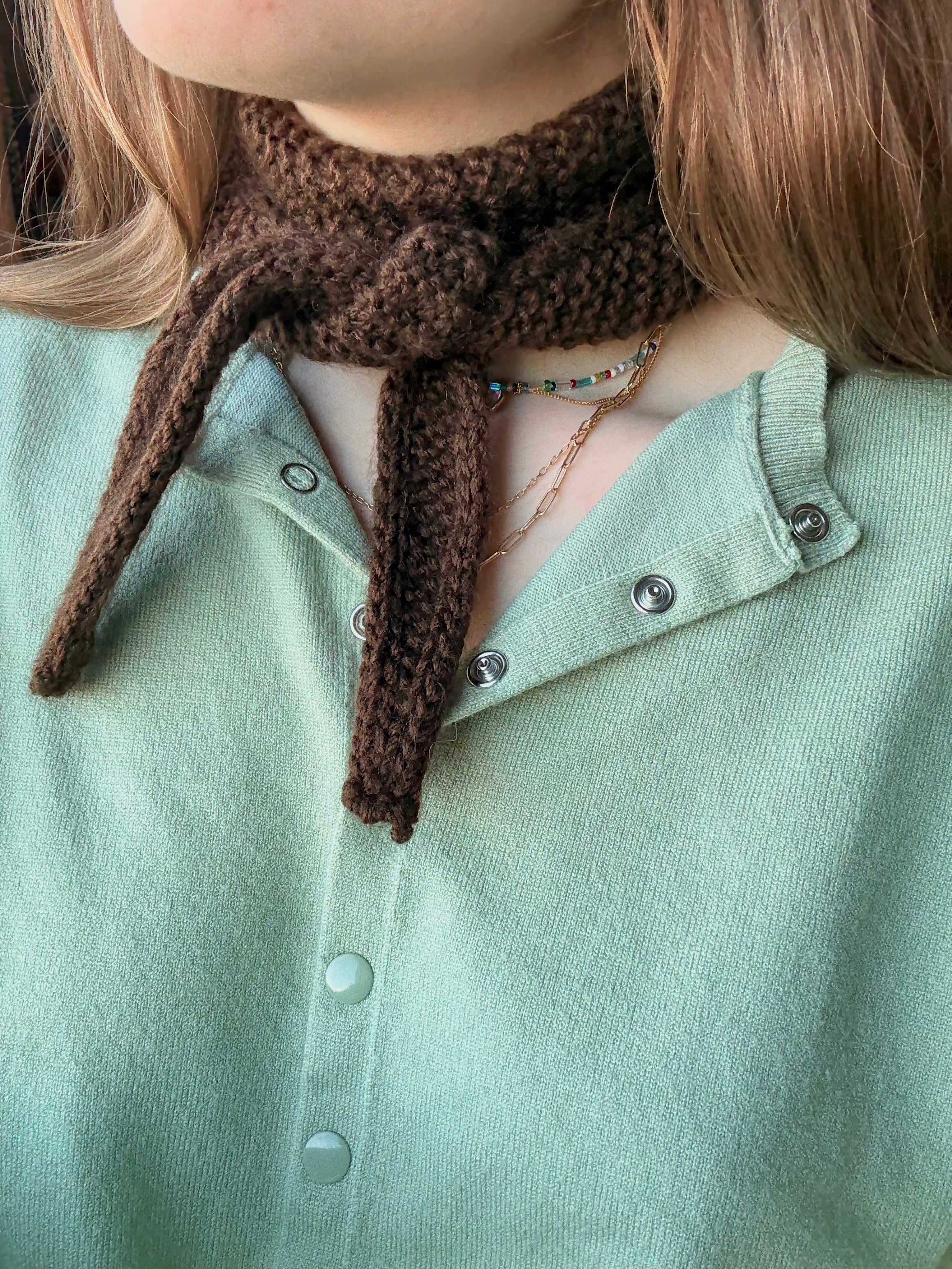 Person wearing a brown knitted scarf with a green shirt