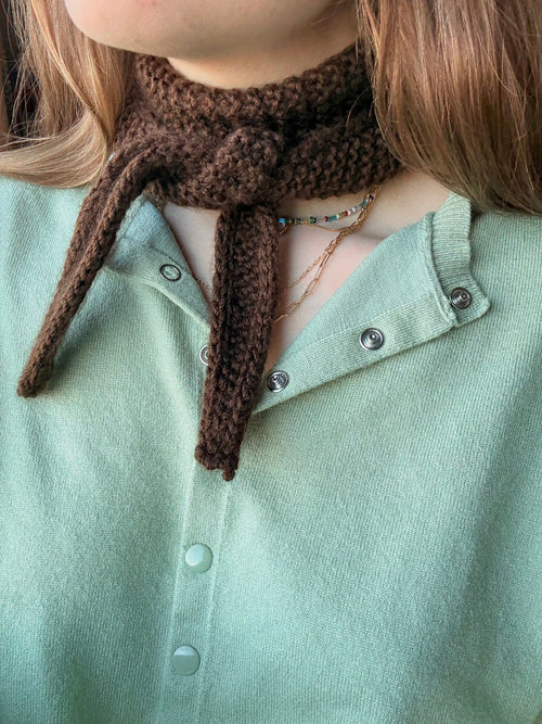 Person wearing a brown knitted scarf with a green shirt